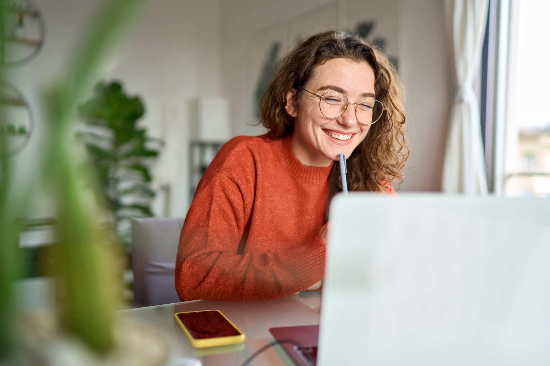 Young happy woman student using laptop watching webinar writing at home.